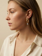 Woman wearing handcrafted gold filigree statement earrings with organic-shaped grey pearls, styled with a professional ivory shirt.