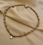 Close-up of a gold beaded choker necklace featuring a single white AAA grade oval pearl pendant