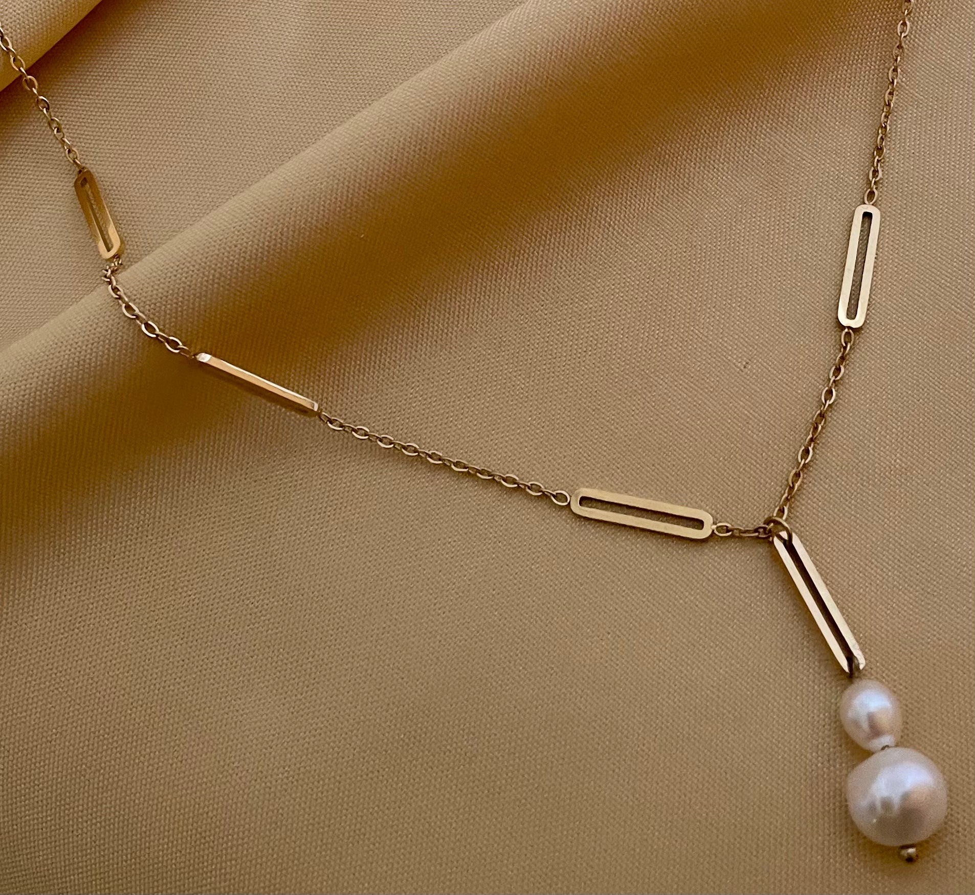 Elegant gold lariat style necklace with genuine freshwater baroque pearls. Minimalist bridal jewelry on a female model, highlighting high-luster pearl drop and modern gold link chain design