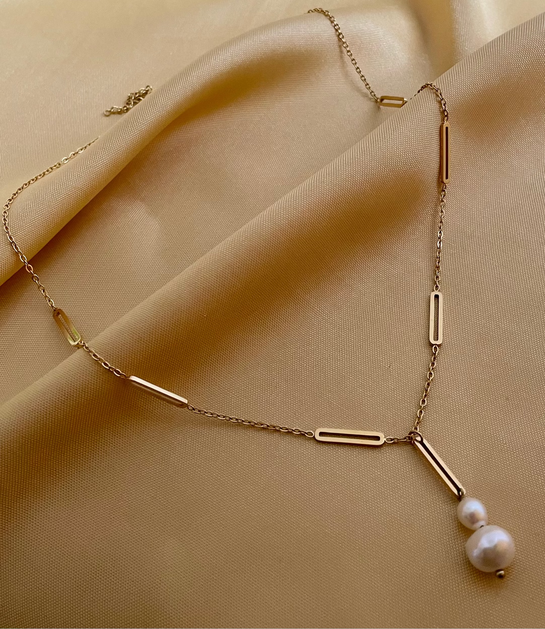 Elegant gold lariat style necklace with genuine freshwater baroque pearls. Minimalist bridal jewelry on a female model, highlighting high-luster pearl drop and modern gold link chain design