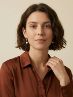 front profile of a woman with short wavy hair wearing elegant gold knot earrings with a suspended white pearl. The lighting highlights the luster of the pearl and the gold finish