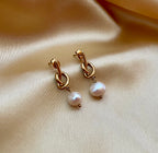 Close-up of gold drop earrings featuring a unique knot design and a dangling white round pearl.
