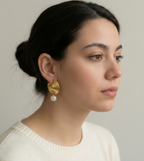 Close-up of ribbed yellow gold shell earrings featuring a round white pearl drop, worn by a model with beautiful hair.