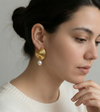 Close-up of ribbed yellow gold shell earrings featuring a round white pearl drop, worn by a model with open hair.
