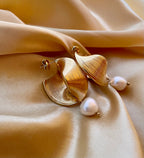 Close-up of ribbed yellow gold shell earrings featuring a round white pearl drop, worn by a model with open hair.