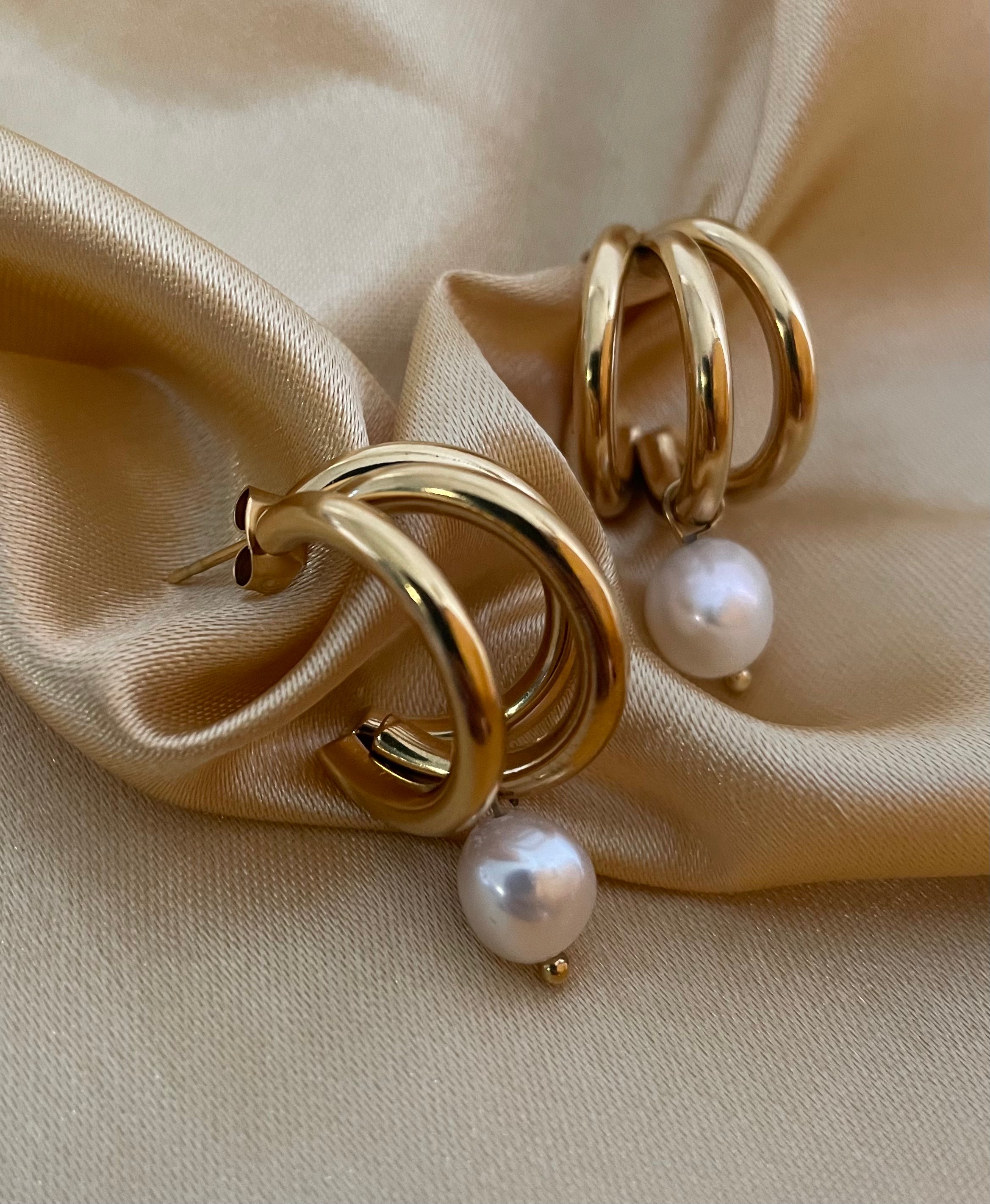 Macro detail of high-luster white pearl charm attached to a polished gold triple-row hoop earring