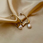 Gold hoop earrings with pearl drops on a beige fabric background