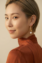 Woman wearing gold hoop earrings with a pearl against a neutral background