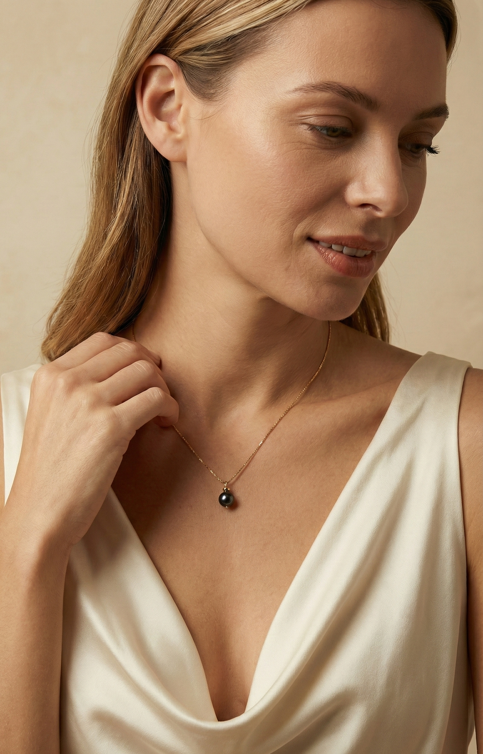 Elegant black pearl solitaire necklace on a twisted gold chain. Luxury jewelry editorial photography featuring a woman in a cream silk blouse with soft studio lighting.