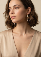 Femme portant des boucles d'oreilles pendantes en perles baroques roses sur une chaîne en or, style parisien