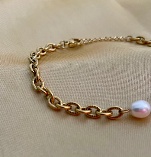Gold chain bracelet with a pearl on a beige fabric background