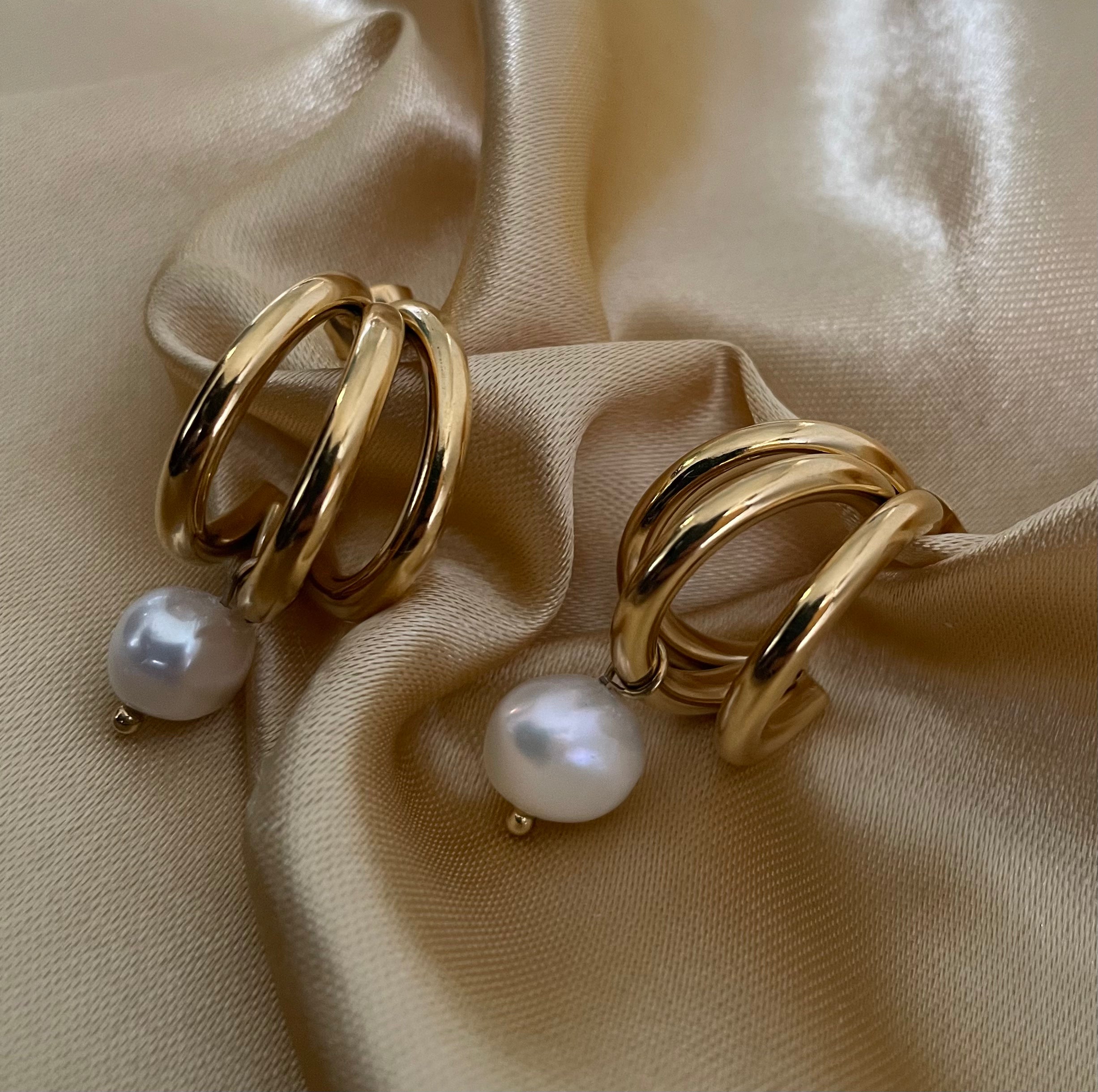 Macro detail of high-luster white pearl charm attached to a polished gold triple-row hoop earring