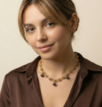 Close-up of a gold knotted link chain necklace featuring three dangling black pearl charms, worn by a model in a brown silk shirt.