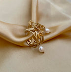 Close-up of a detailed gold openwork hoop earrings featuring a leaf motif and a single dangling white oval pearl.