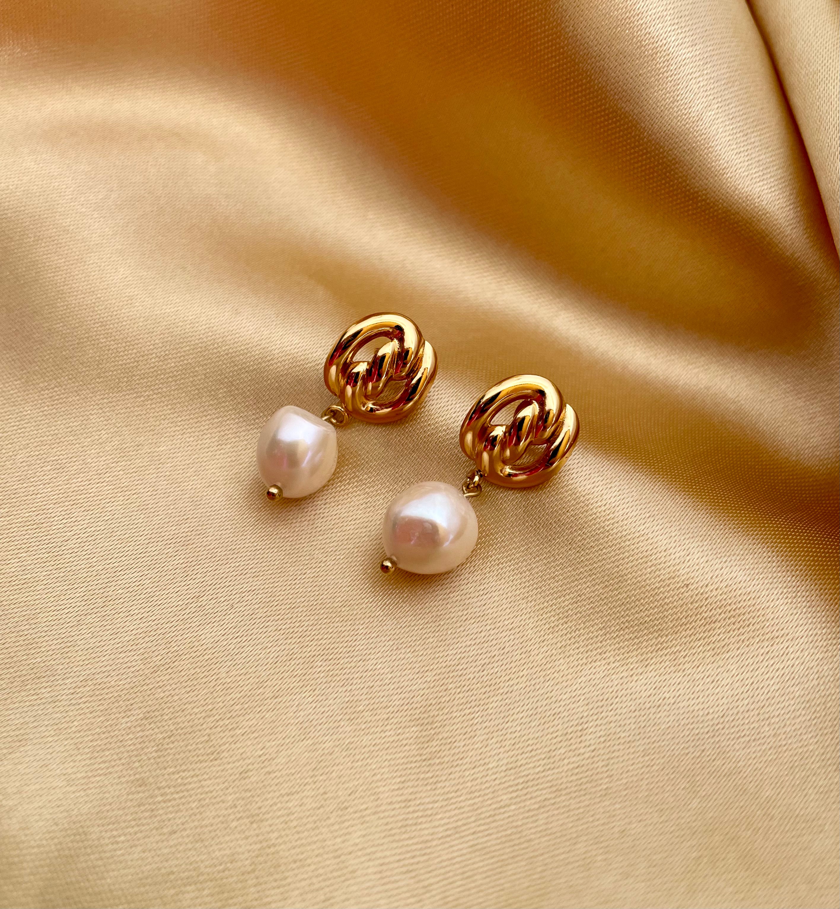 Gold pearl drop earrings featuring a chunky gold knot design and genuine white pearls. Modeled on an ear to show scale and fit