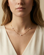 Close-up of a dainty gold chain necklace featuring three small, oval champagne pearls and gold spacer beads, worn by a model in an ivory silk top