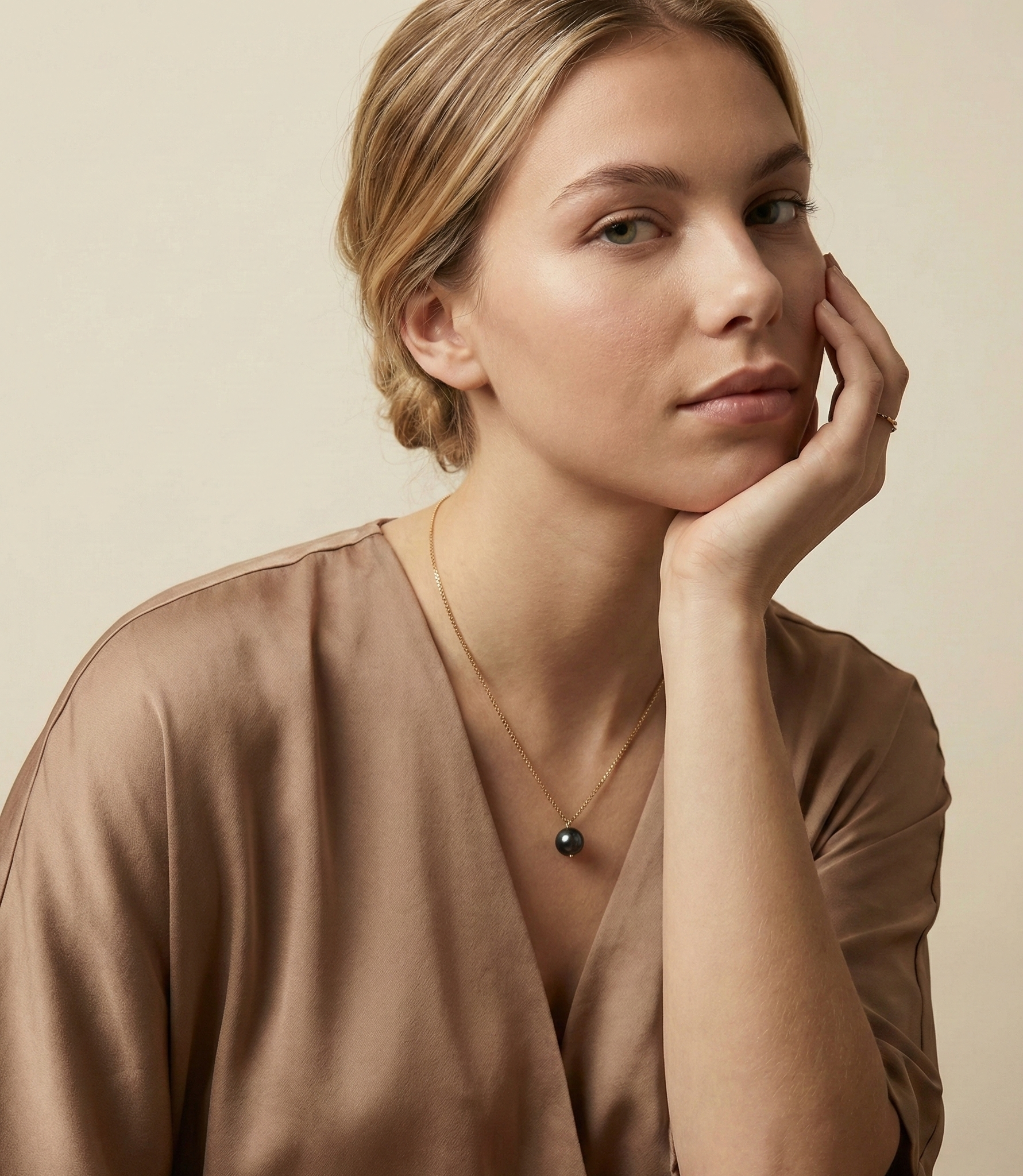 Dainty gold necklace featuring a single lustrous black pearl charm, displayed in a luxury jewelry portrait