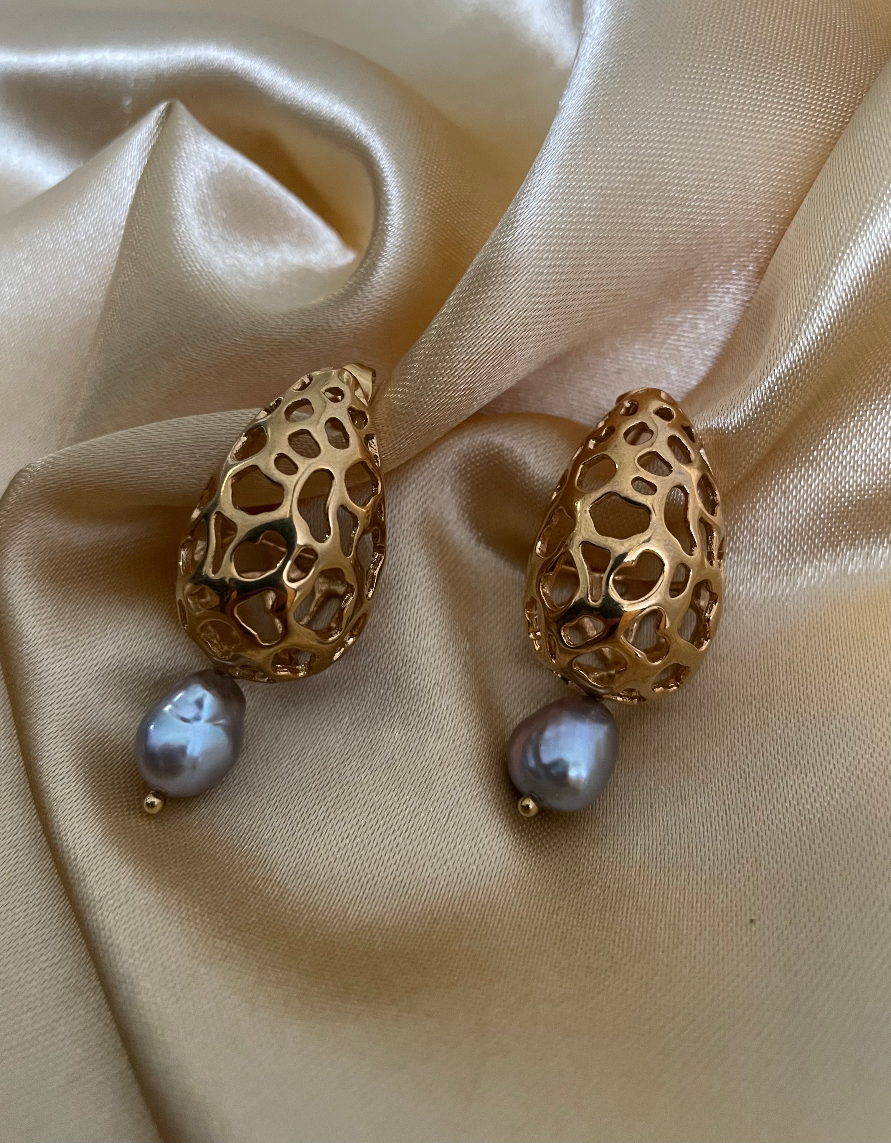 High-resolution editorial jewelry portrait featuring a model wearing intricate gold mesh and grey pearl drop earrings with warm studio lighting.