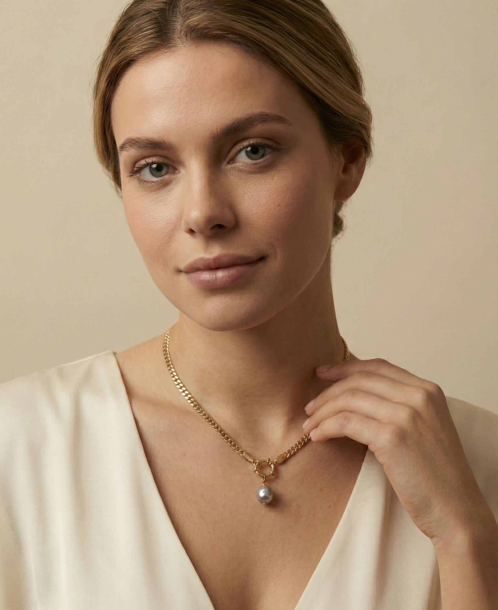 Close-up editorial shot of a woman wearing a minimalist gold chain with a grey baroque pearl drop, highlighting the necklace length and luster against warm skin tones.