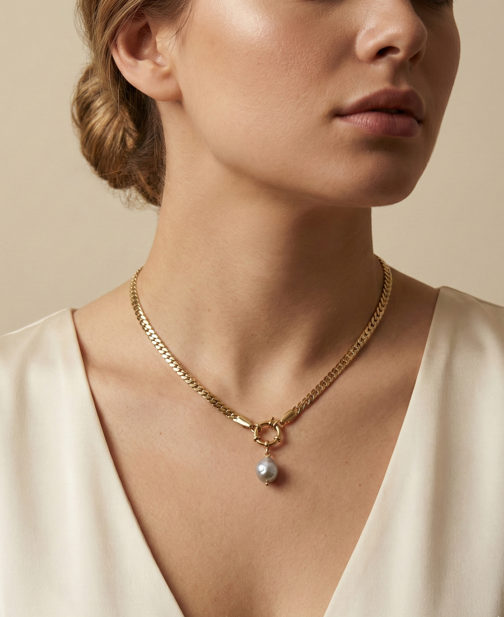 Close-up editorial shot of a woman wearing a minimalist gold chain with a grey baroque pearl drop, highlighting the necklace length and luster against warm skin tones
