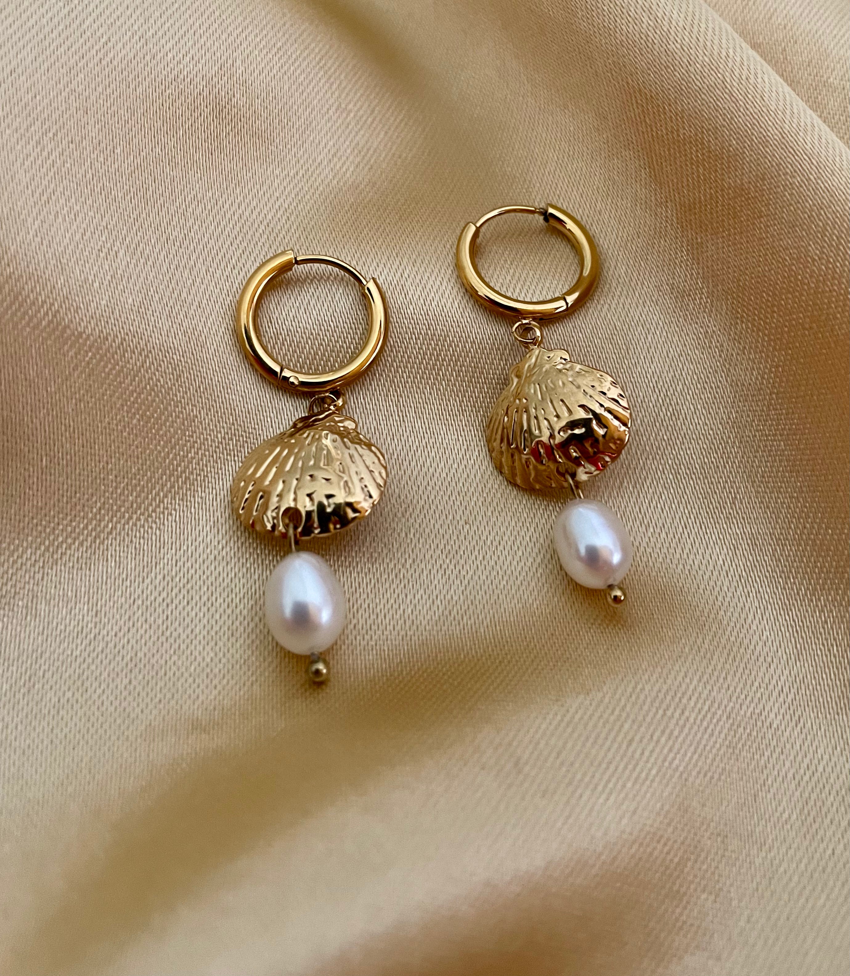 French style inspiration: textured gold sea shell huggie earrings with a dainty pearl charm. Soft studio lighting highlights the iridescence of the pearl 