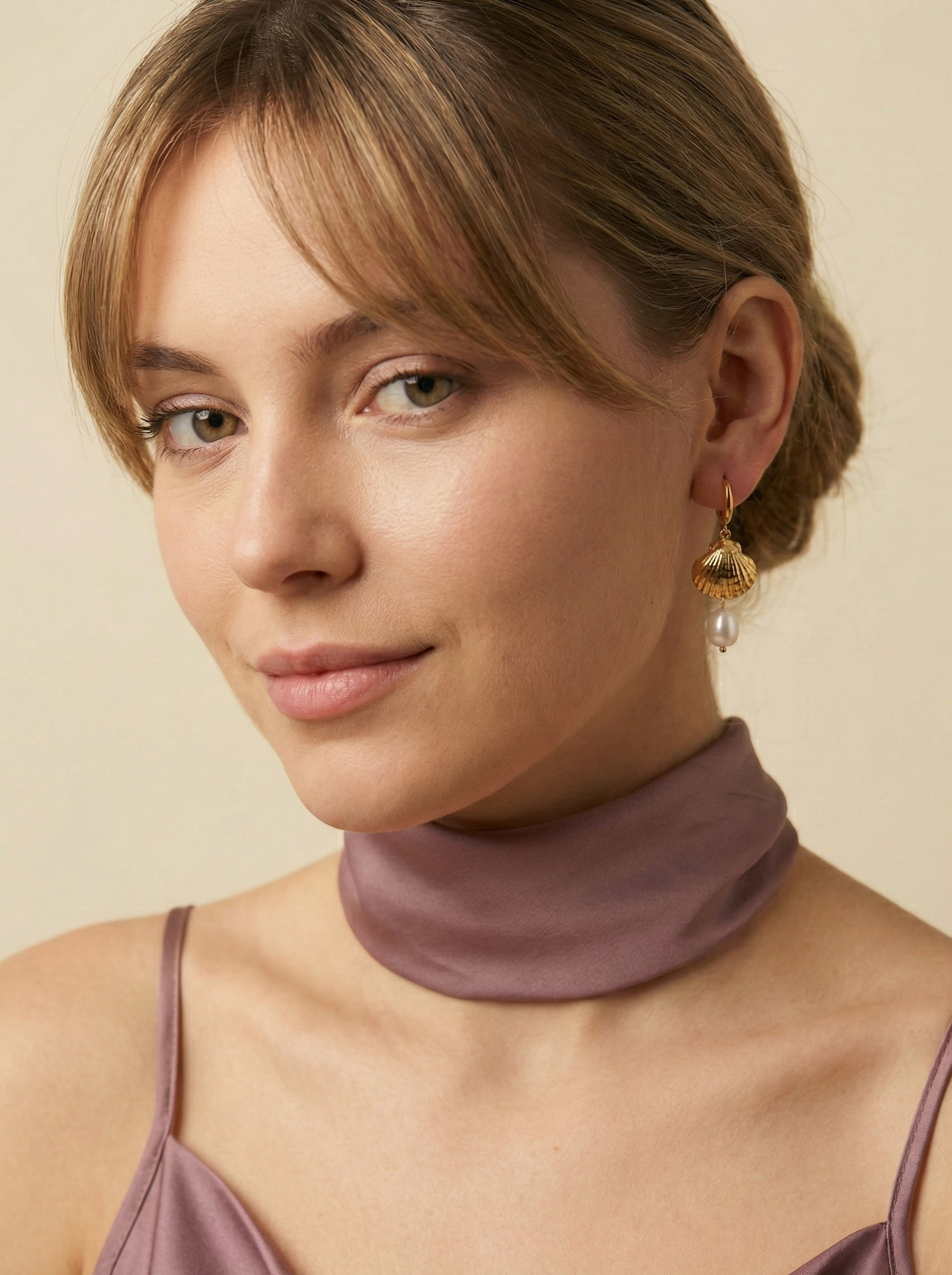 Close-up detail of gold scallop shell earrings featuring a lustrous white pearl drop. The earrings are worn by a model to show scale, highlighting the textured gold finish and elegant dangle design perfect for beach weddings or summer luxury
