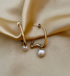 Gold hoop earrings with pearl drops on a beige fabric background
