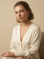 Editorial close-up of a model in a Parisian chic style wearing an ivory silk shirt. She is wearing unique, organic-shaped gold earrings featuring lustrous pink oval pearl drops