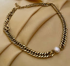 Gold chain necklace with a pearl pendant on a beige fabric background