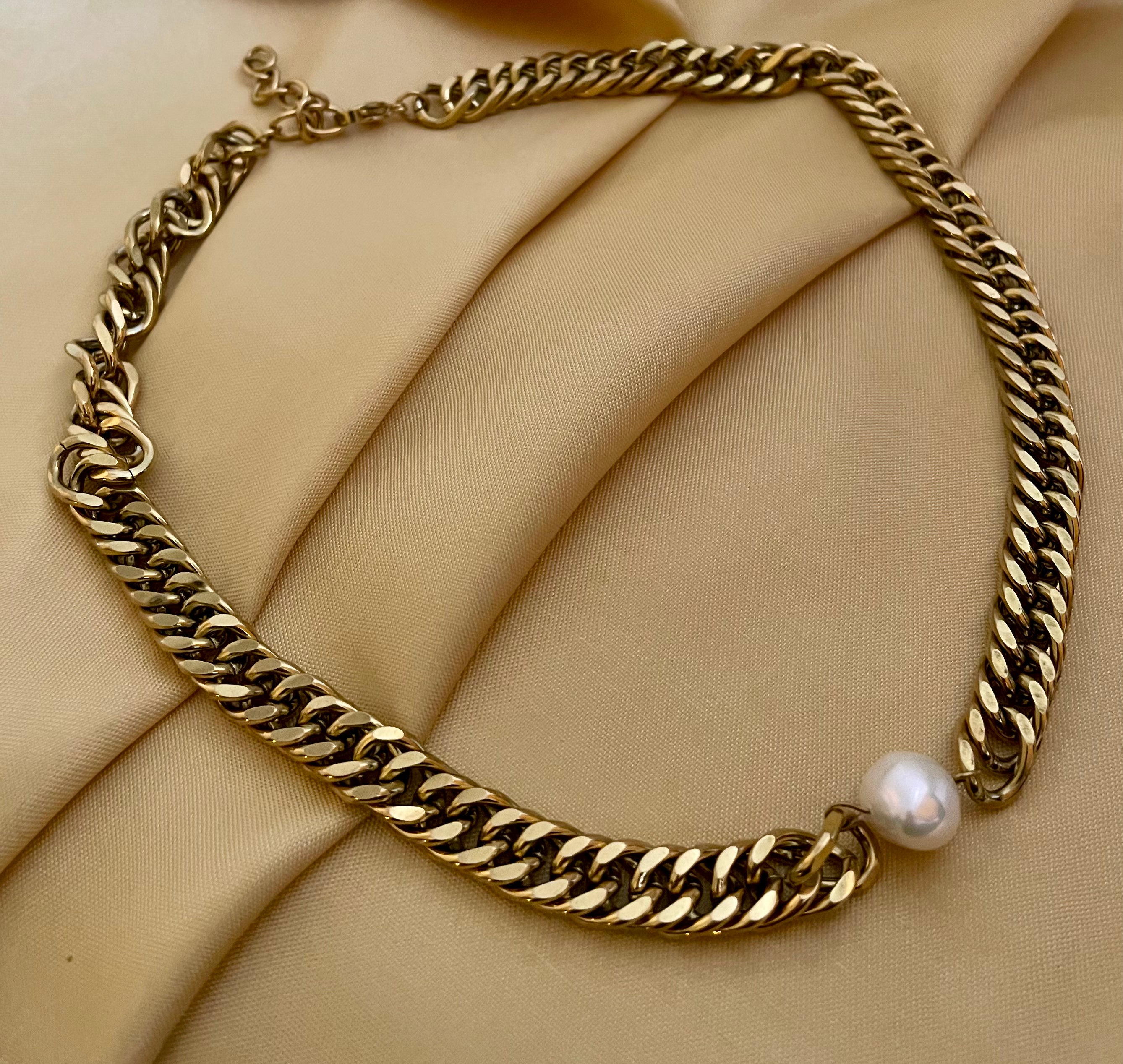 Gold chain necklace with a pearl pendant on a beige fabric background