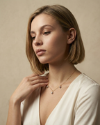 Close-up detail of a delicate gold chain necklace featuring three small metallic grey baroque pearls with high luster, draped elegantly on a woman's collarbone against an ivory silk top. High-resolution jewelry photography highlighting the pearl texture and dainty chain links