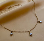 Close-up detail of a delicate gold chain necklace featuring three small metallic grey baroque pearls with high luster. High-resolution jewelry photography highlighting the pearl texture and dainty chain links