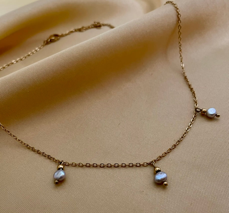 Close-up detail of a delicate gold chain necklace featuring three small metallic grey baroque pearls with high luster. High-resolution jewelry photography highlighting the pearl texture and dainty chain links