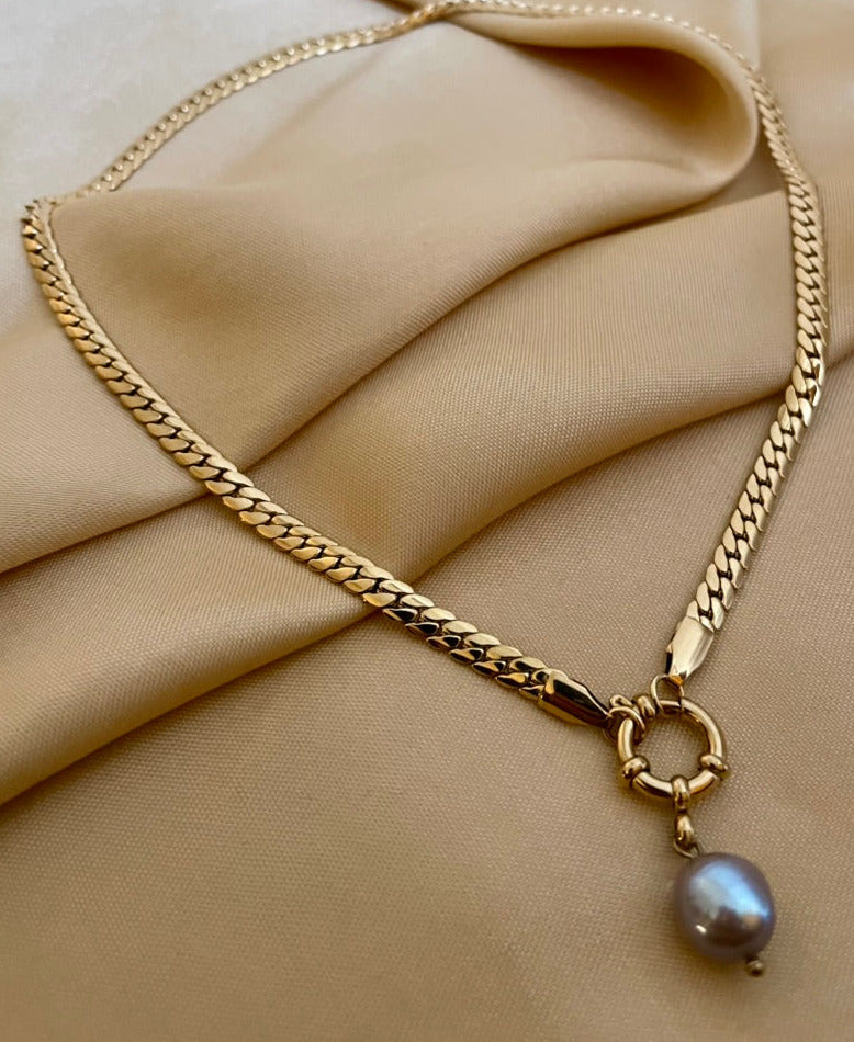 Model wearing a gold curb chain necklace featuring a single grey baroque pearl pendant with a front toggle clasp, styled with an ivory silk top
