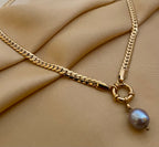 Model wearing a gold curb chain necklace featuring a single grey baroque pearl pendant with a front toggle clasp, styled with an ivory silk top