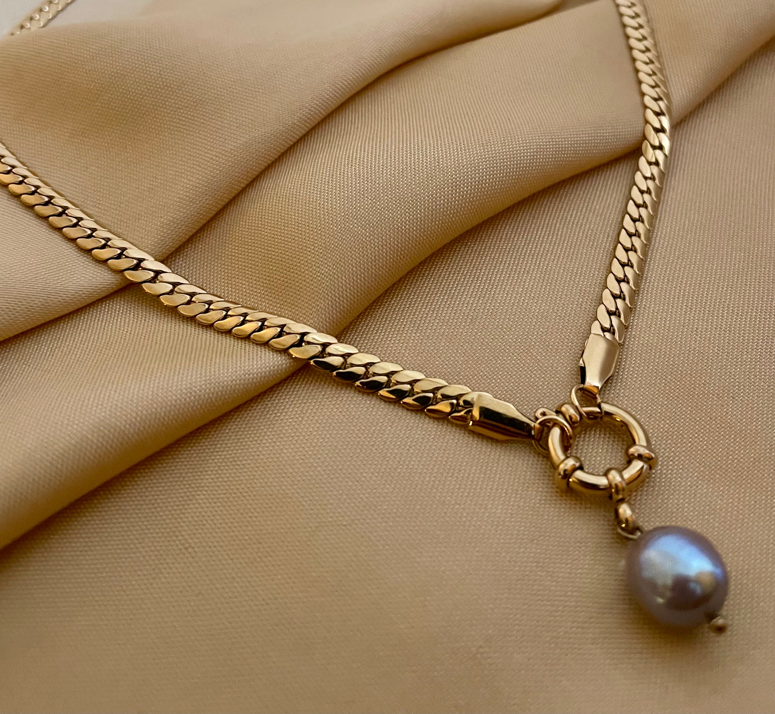 Model wearing a gold curb chain necklace featuring a single grey baroque pearl pendant with a front toggle clasp, styled with an ivory silk top
