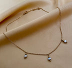 Close-up detail of a delicate gold chain necklace featuring three small metallic grey baroque pearls with high luster. High-resolution jewelry photography highlighting the pearl texture and dainty chain links