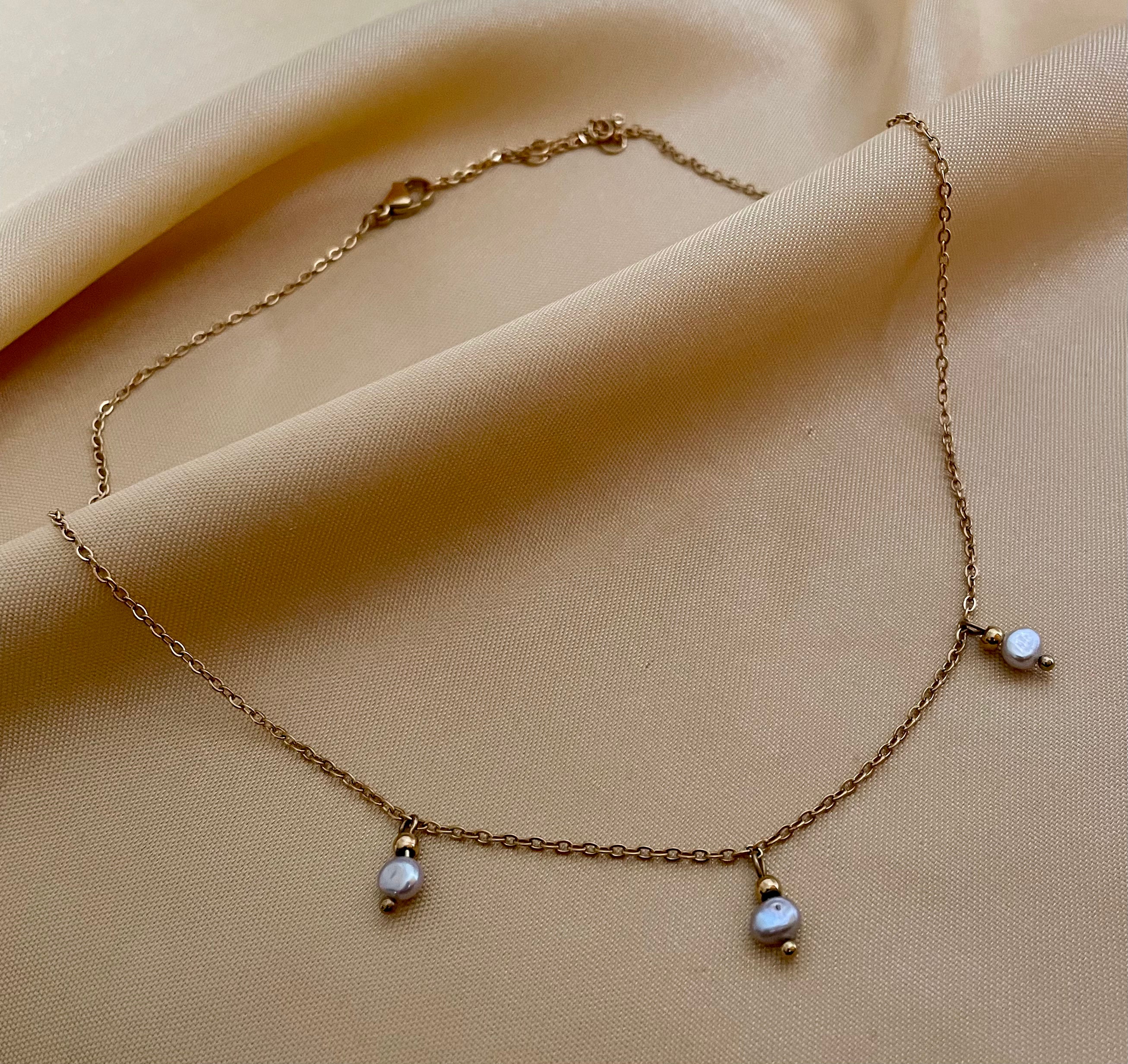 Close-up detail of a delicate gold chain necklace featuring three small metallic grey baroque pearls with high luster. High-resolution jewelry photography highlighting the pearl texture and dainty chain links