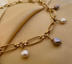Close-up of a gold link chain necklace featuring dangling white and grey baroque pearl charms on a model wearing an ivory coa
