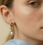 Close-up of gold chain link earrings featuring a lustrous oval white pearl drop. The earrings are shown on a model to demonstrate scale, featuring a high-polish gold finish and organic pearl shape