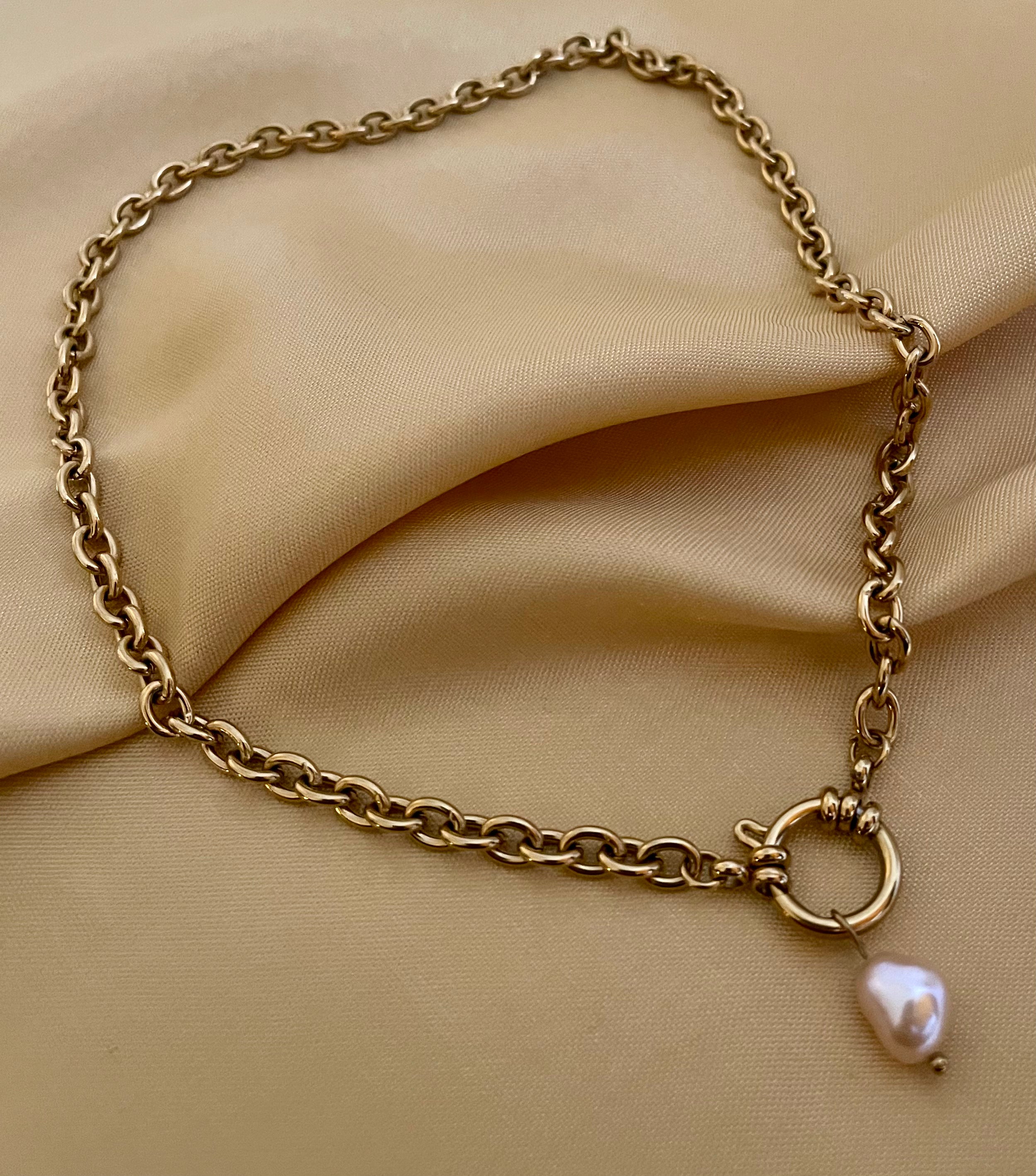 Close-up of a gold link chain necklace featuring a front toggle clasp and a single pink baroque pearl pendant. The high-luster pearl hangs elegantly from the gold ring closure