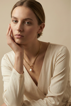 Model wearing an elegant gold chain necklace with a white baroque pearl drop and front clasp detail, styled with an ivory silk V-neck top