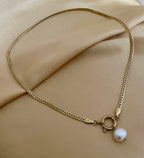 lose-up detail of a flat gold curb chain necklace featuring a lustrous white baroque pearl pendant attached to a round front spring clasp