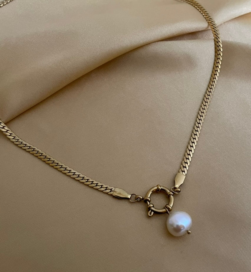 Close-up detail of a flat gold curb chain necklace featuring a lustrous white baroque pearl pendant attached to a round front spring clasp