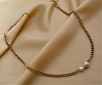 Close-up of a model wearing a dainty gold curb chain necklace featuring a pink baroque pearl and a small champagne pearl, styled with an ivory silk top