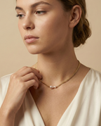 Close-up of a model wearing a dainty gold curb chain necklace featuring a pink baroque pearl and a small champagne pearl, styled with an ivory silk top
