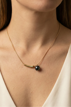 Elegant gold curved bar necklace with black pearl pendant worn by a model. Minimalist jewelry design featuring a high-luster round black pearl and sleek gold spacer on a delicate chain