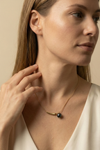 Elegant gold curved bar necklace with black pearl pendant worn by a model. Minimalist jewelry design featuring a high-luster round black pearl and sleek gold spacer on a delicate chain