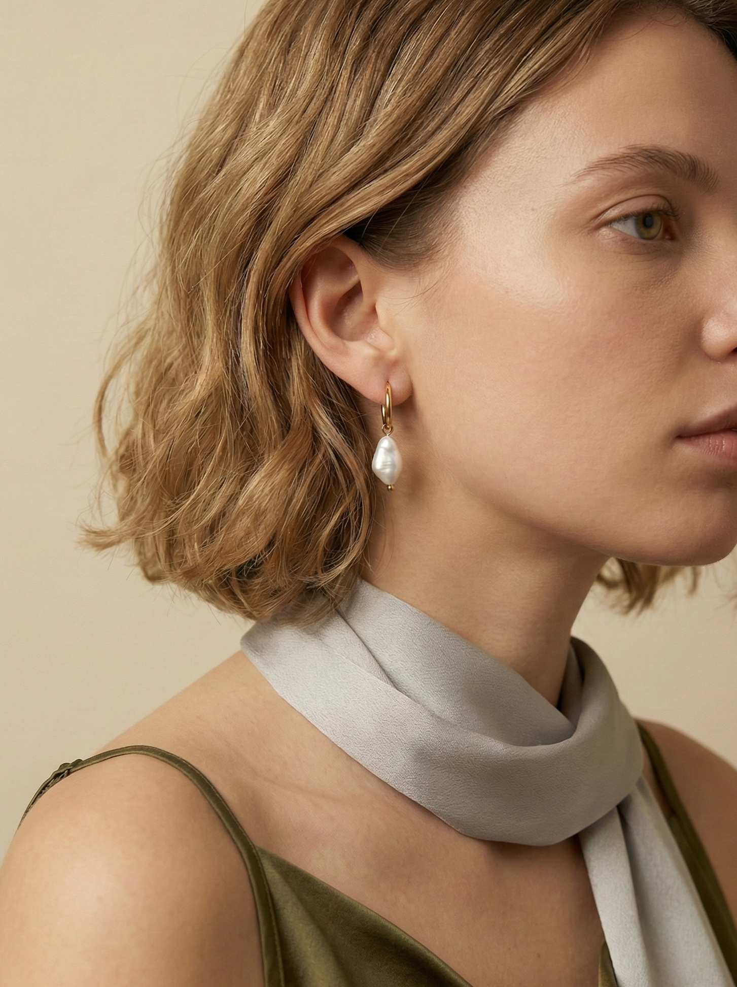 Minimalist 18k gold huggie hoop earrings with saltwater keshi baroque pearl charms. Elegant French-style bridal jewelry modeled on a woman with a low bun, highlighting the classic drop earring design and warm beige aesthetic.