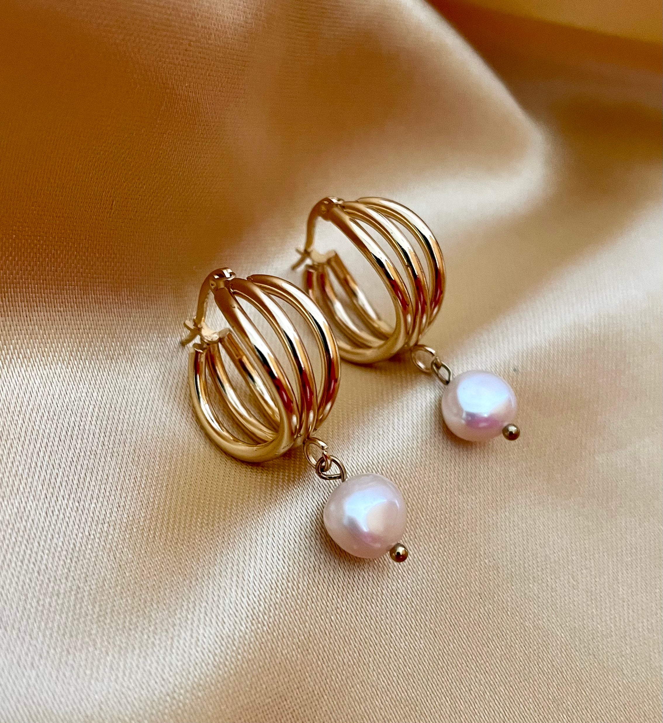 Luxury gold huggie earrings with white baroque pearl drop on model ear. High-luster freshwater pearl jewelry with triple-split gold hoop design in an editorial close-up